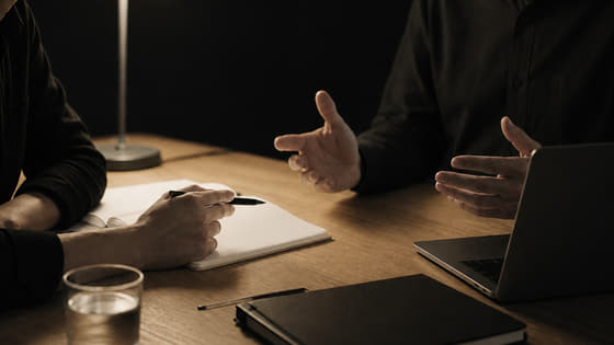 Deux dirigeants en discussion autour d’une table de travail, éclairés par une lampe.