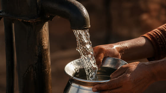 Mains recueillant l’eau d’une pompe manuelle dans un récipient de métal.