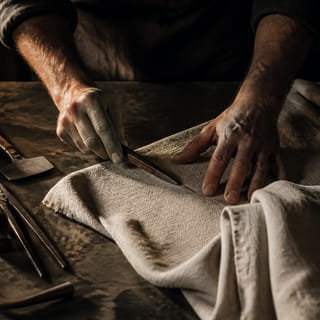 A craftsman’s hands working linen beside their tools.
